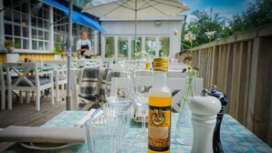 An outdoor dining area with a table set for two, featuring a bottle of beverage, a salt shaker, and a vase with flowers. - Turistgården - House Of Ven (Sankt Ibb)