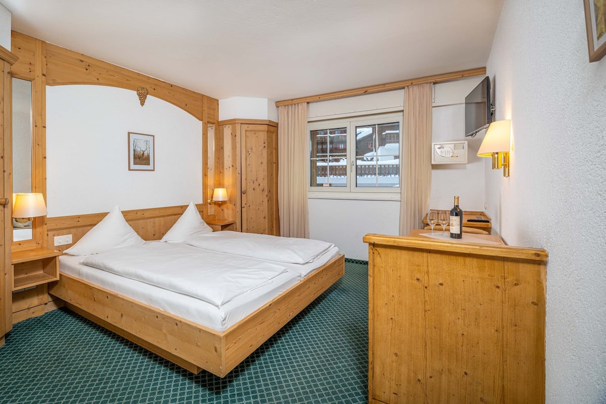 Dormitorio con estructura de madera, una cama, lámparas de noche, un tocador y una ventana con vistas a un paisaje nevado.