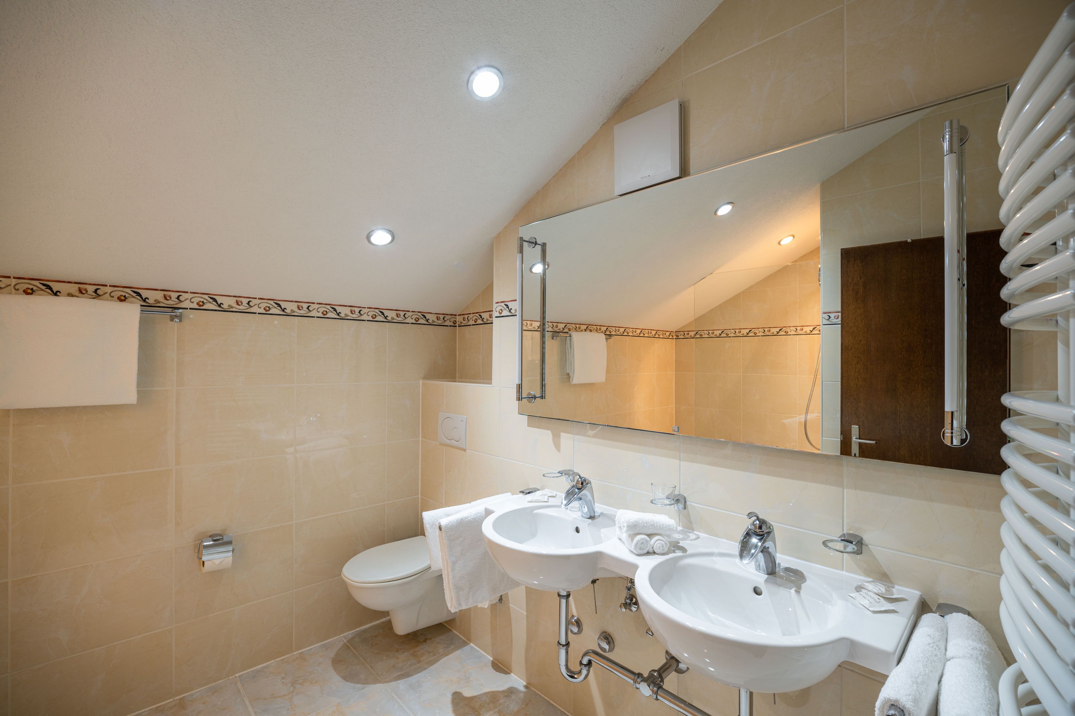 Un baño moderno con dos lavamanos, un inodoro y un espejo grande.