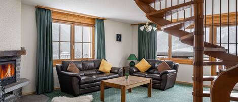 A cozy living room with a fireplace, leather sofas, a wooden coffee table, and a spiral staircase.