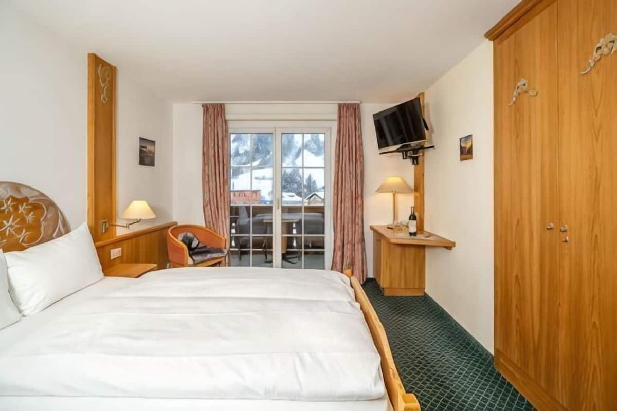 Una habitación de hotel con cama, escritorio, silla, televisor montado en la pared y armario.