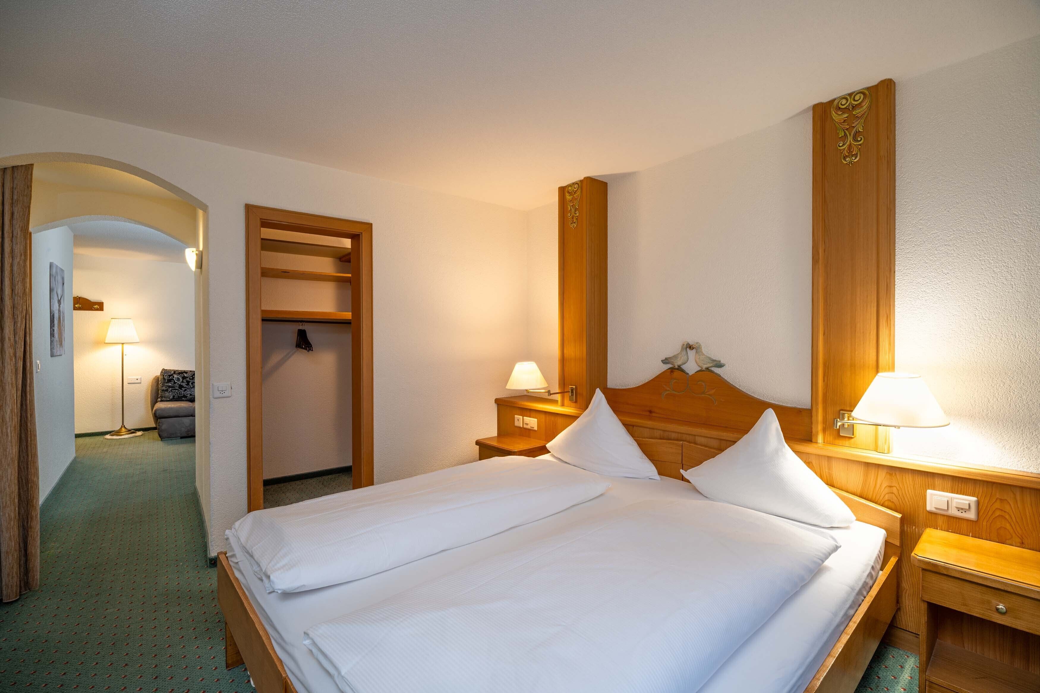 A hotel room with a large bed, two bedside tables with lamps, a wooden headboard, and a wardrobe.