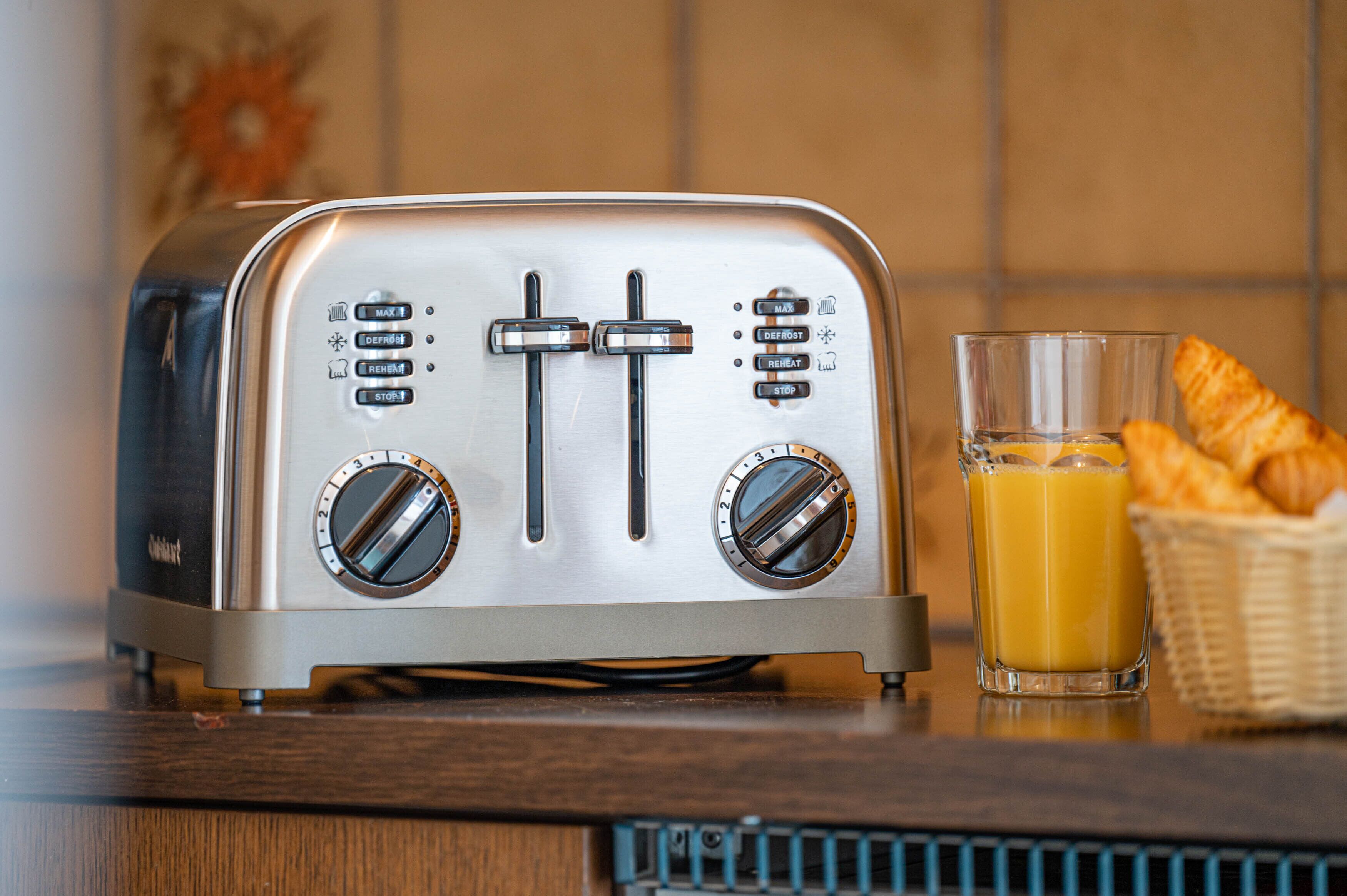 A vintage toaster with two dials and a glass of orange juice on a wooden surface.
