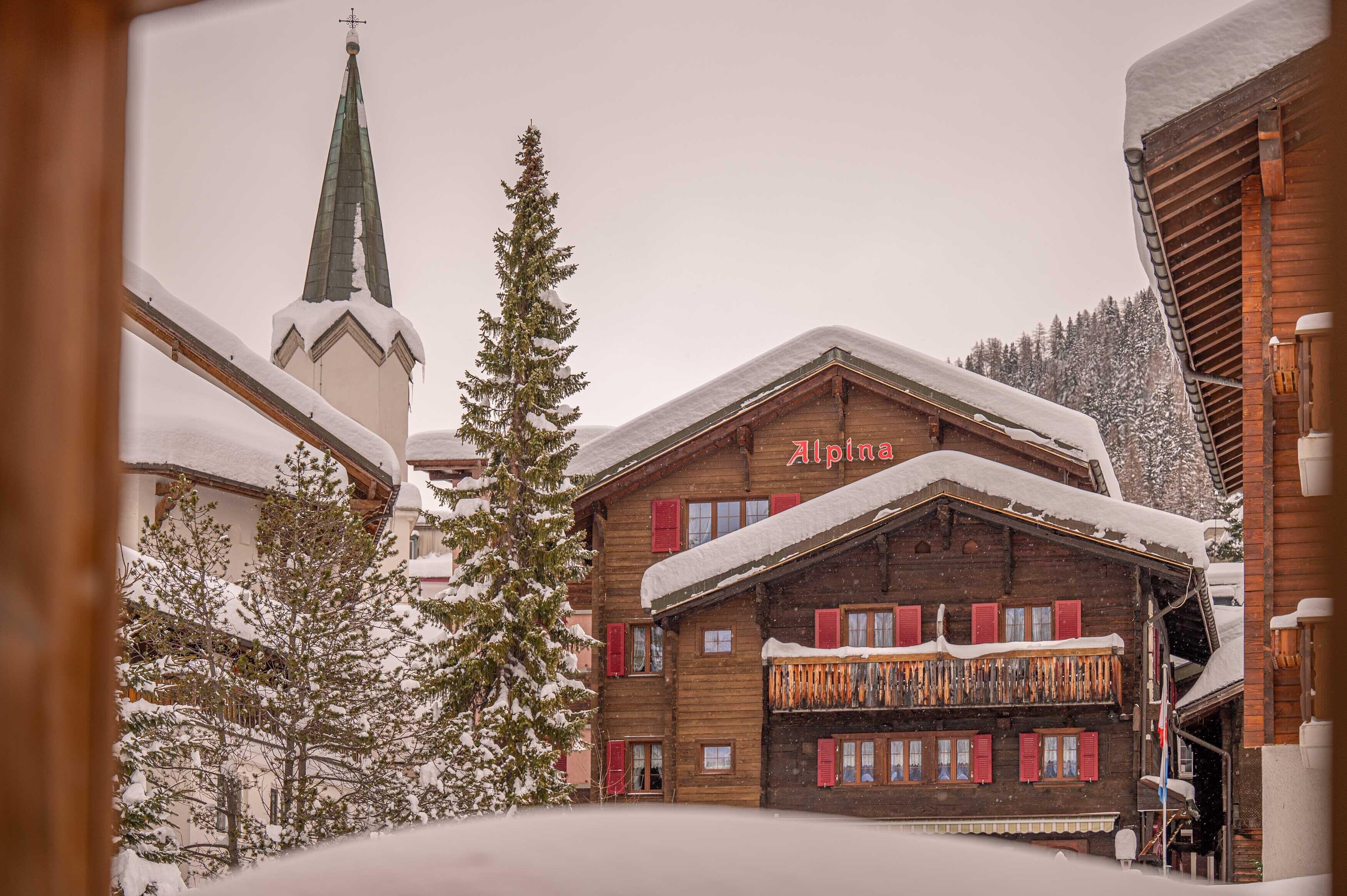 Un bâtiment en bois avec une enseigne indiquant « Alpina » et un toit recouvert de neige.