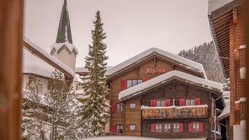 Un bâtiment en bois avec une enseigne indiquant « Alpina » et un toit recouvert de neige.