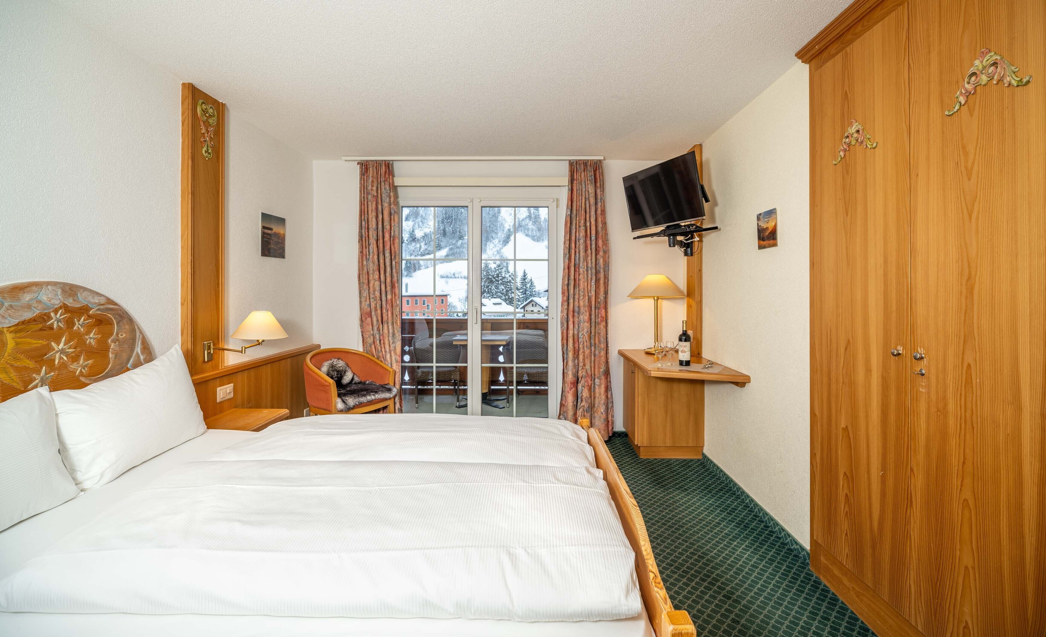 Ein Hotelzimmer mit einem großen Bett, einem Holzschrank, einem Fernseher, einem Schreibtisch mit Lampe und einem Sessel.