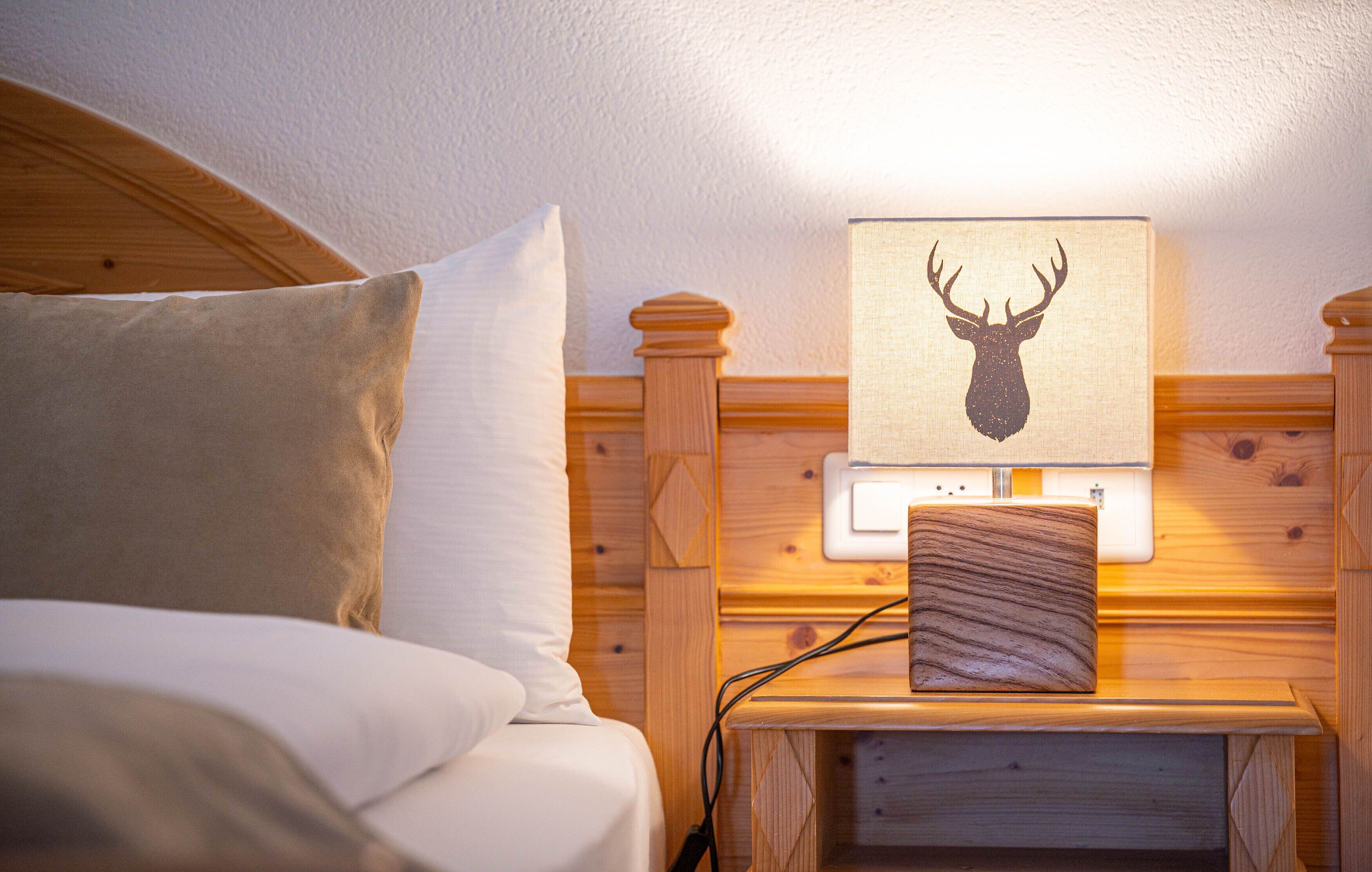 A wooden headboard with a mounted picture of a deer head, a bedside lamp, and a power outlet.