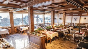 A spacious restaurant with wooden beams, large windows, and a marble floor. Tables are set with white tablecloths and candles. - Grichting Hotel & Serviced Apartments (Leukerbad)