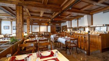 Ein Restaurant mit Holzbalken und einem Buffetbereich. Die Tische sind mit weißen Tischdecken und roten Untersetzern gedeckt.