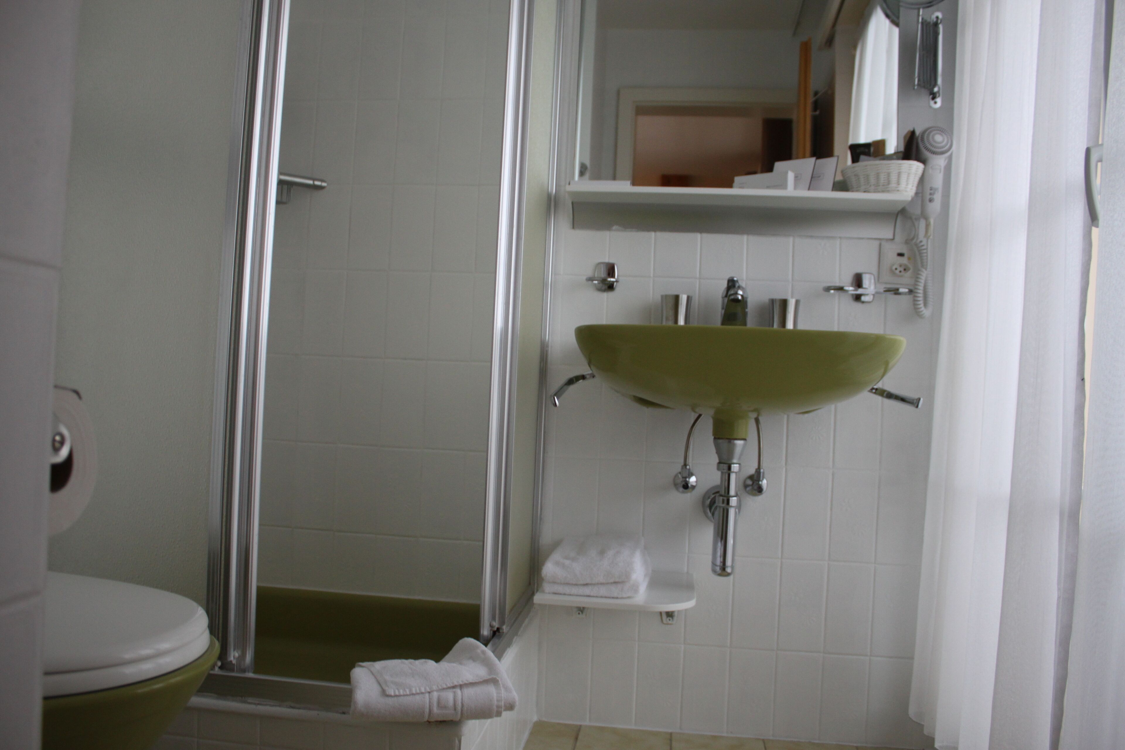 Een badkamer met douche, toilet, wastafel en een spiegel.