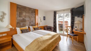 A hotel room with a large bed, a desk with a chair, a television, and a view of the outside. - Grichting Hotel & Serviced Apartments (Leukerbad)