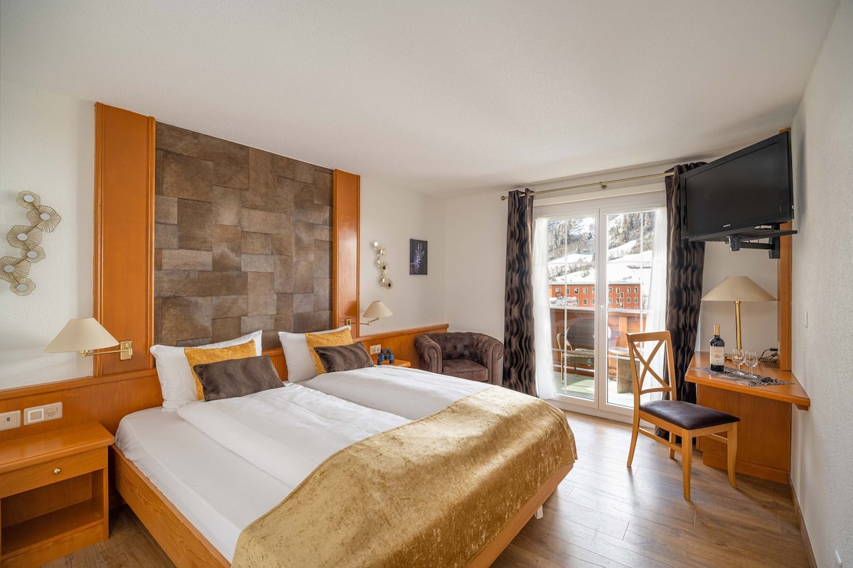 Habitación de hotel con una cama grande, un escritorio con silla, televisión y vistas al exterior.