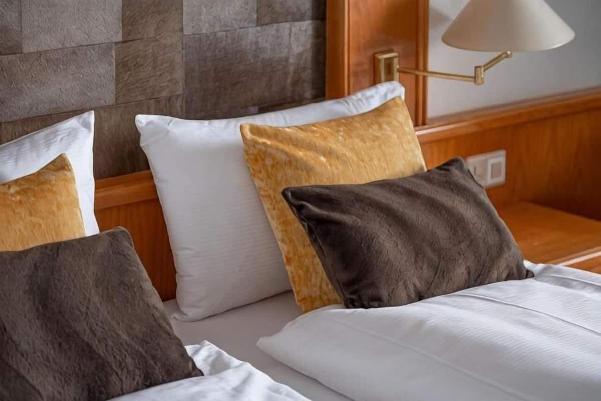 Habitación de hotel con cama, almohadas, lámpara y pared con un diseño texturizado.