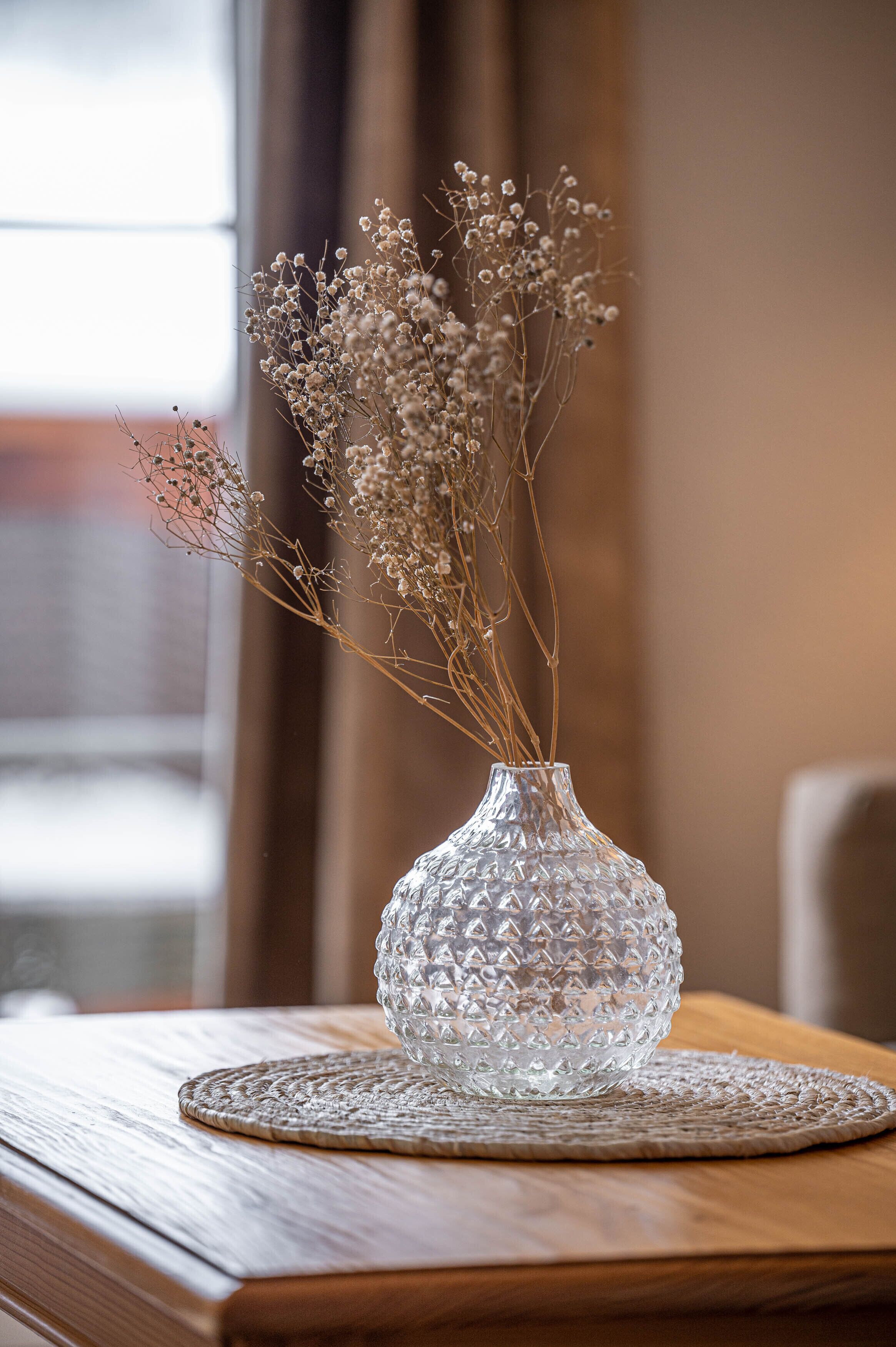 A clear glass vase with dried flowers on a wooden table.