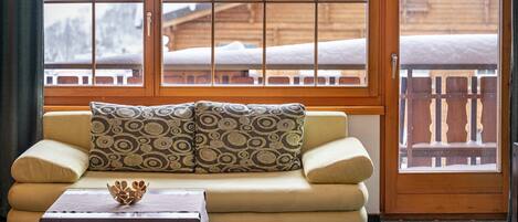 A cozy room with a sofa, a wooden table, and a window with a view of a wooden cabin.