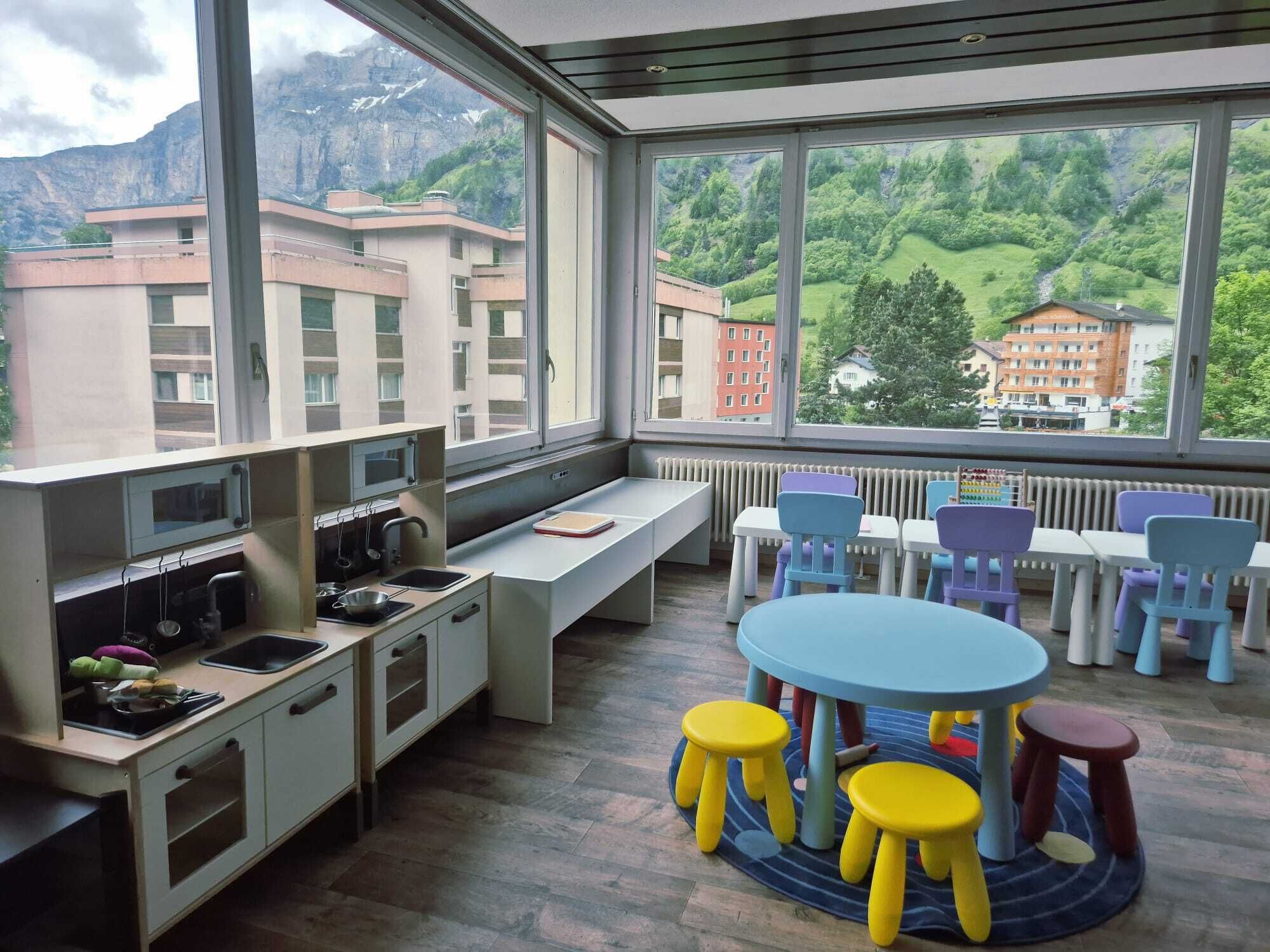 A modern kitchen with a large window, a dining area with colorful stools, and a view of a mountainous landscape.