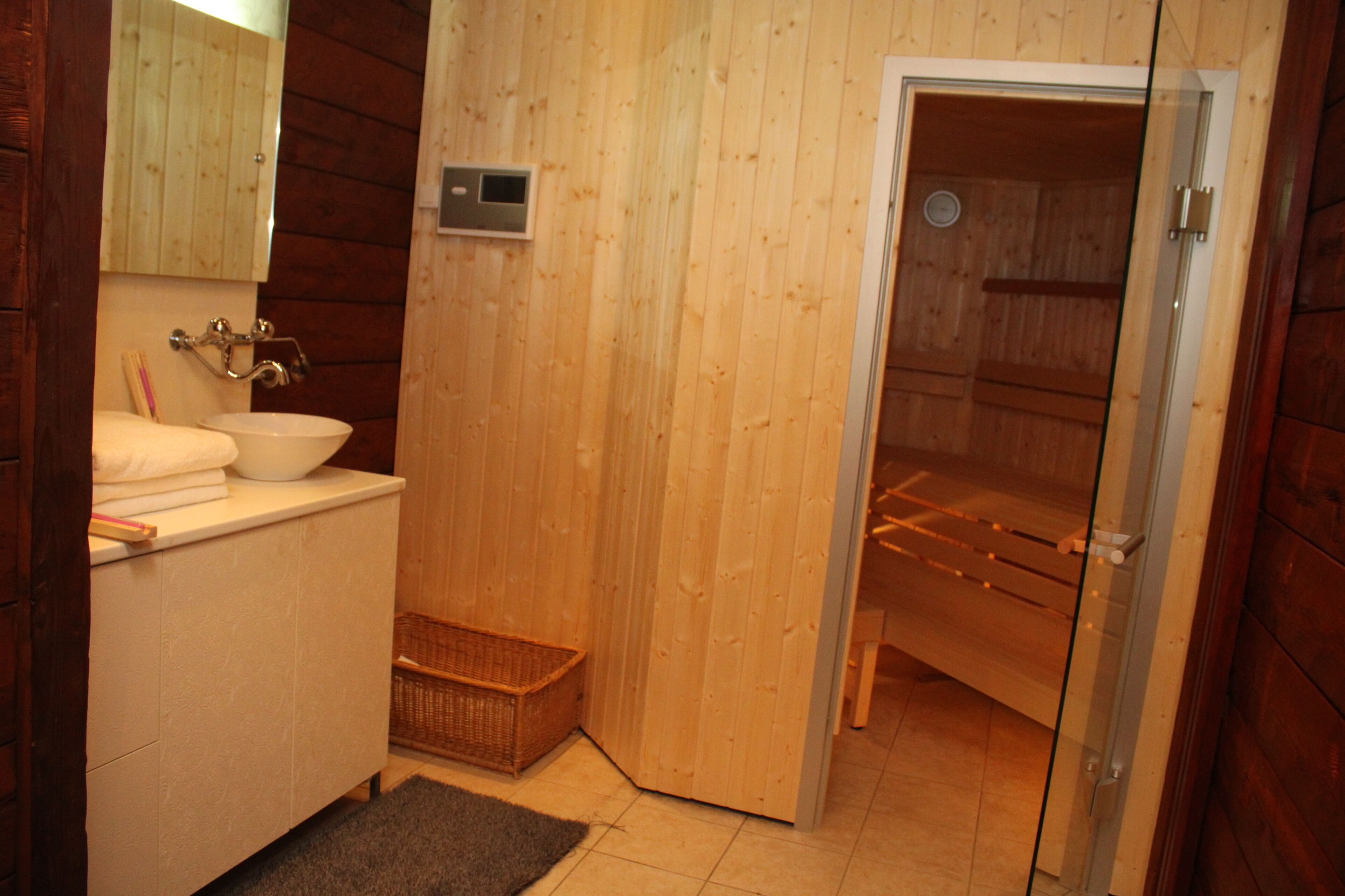 A wooden interior with a white sink, mirror, and a sauna door.