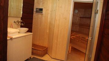 A wooden interior with a white sink, mirror, and a sauna door.