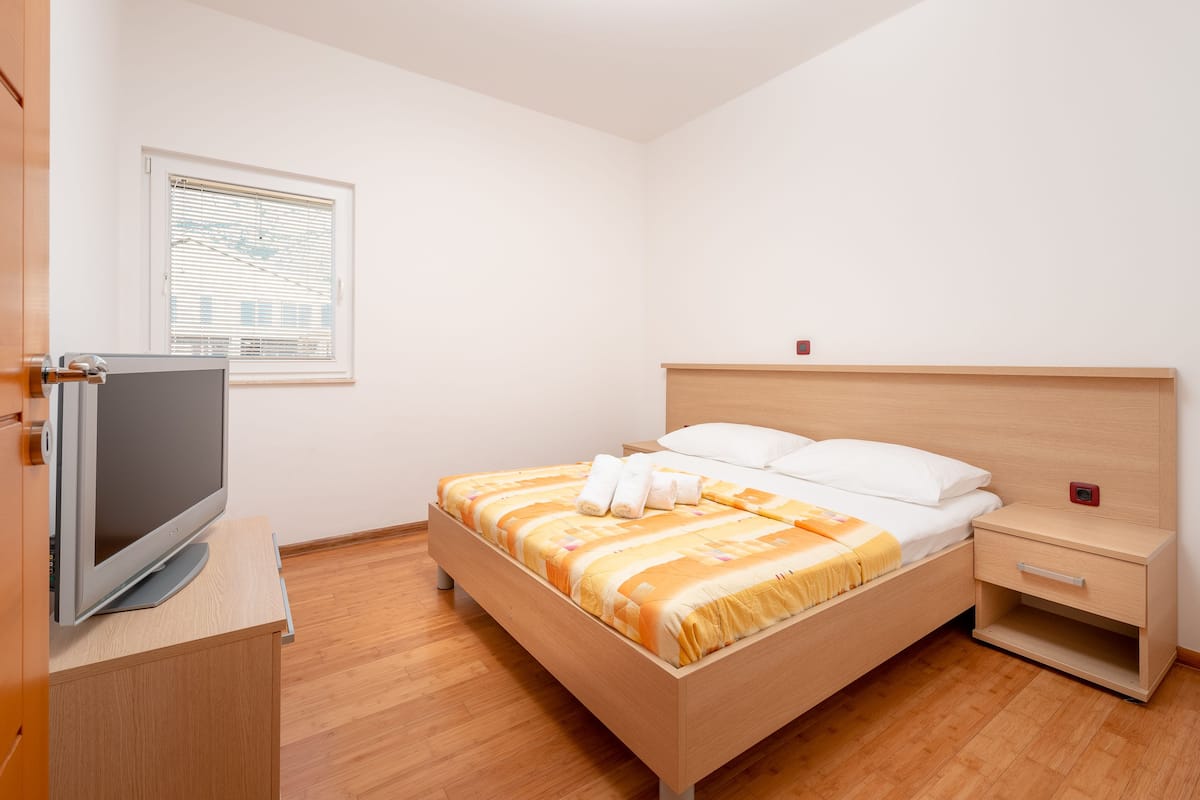 Ein ordentlich eingerichtetes Schlafzimmer mit Bett, Nachttisch und Fernseher auf einem Holzschrank.