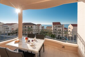 Un balcón con una mesa lista para dos personas, con vistas a la costa, edificios y el mar.