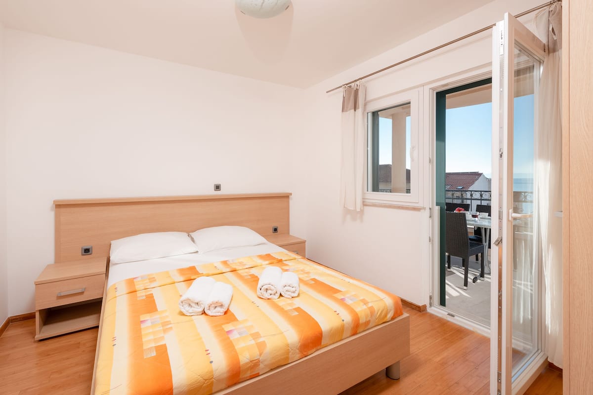 Ein Schlafzimmer mit Bett, Nachttisch, einer Schiebetür zum Balkon und Blick ins Freie.