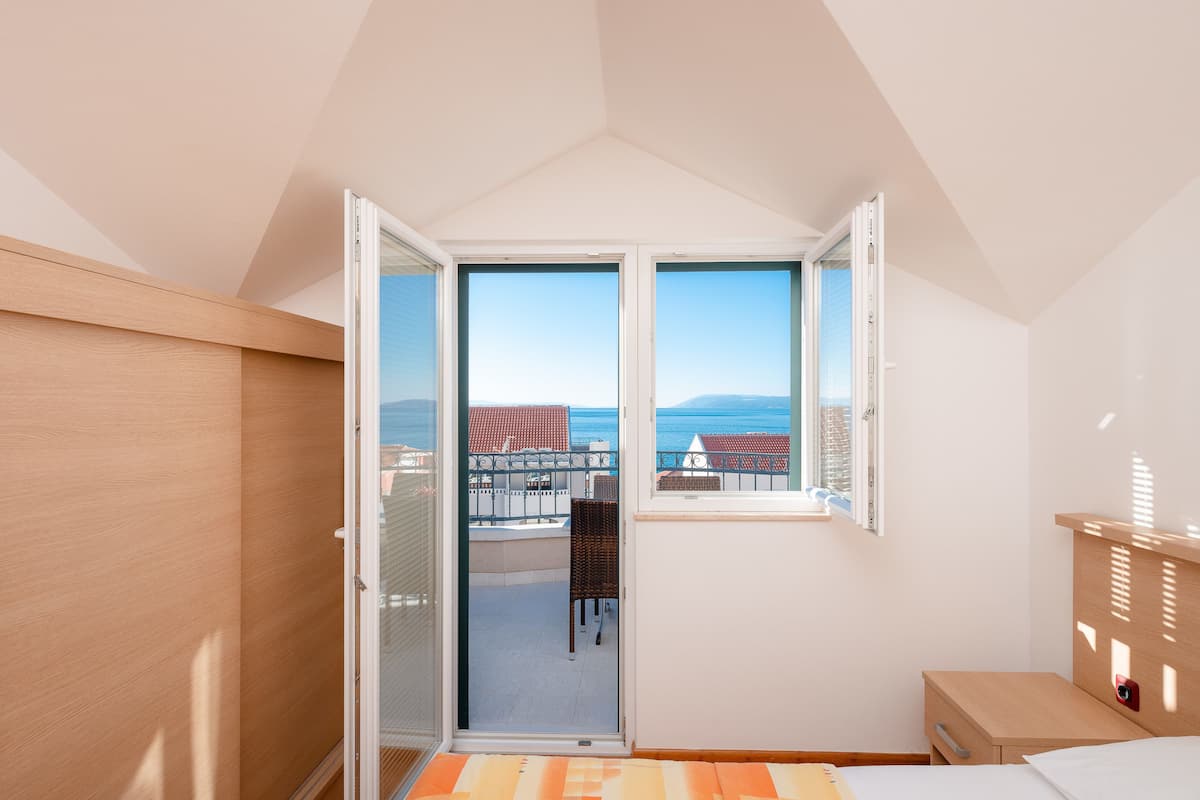 Ein Schlafzimmer mit Balkon, Bett, Nachttisch und Blick auf das Meer und die Gebäude.