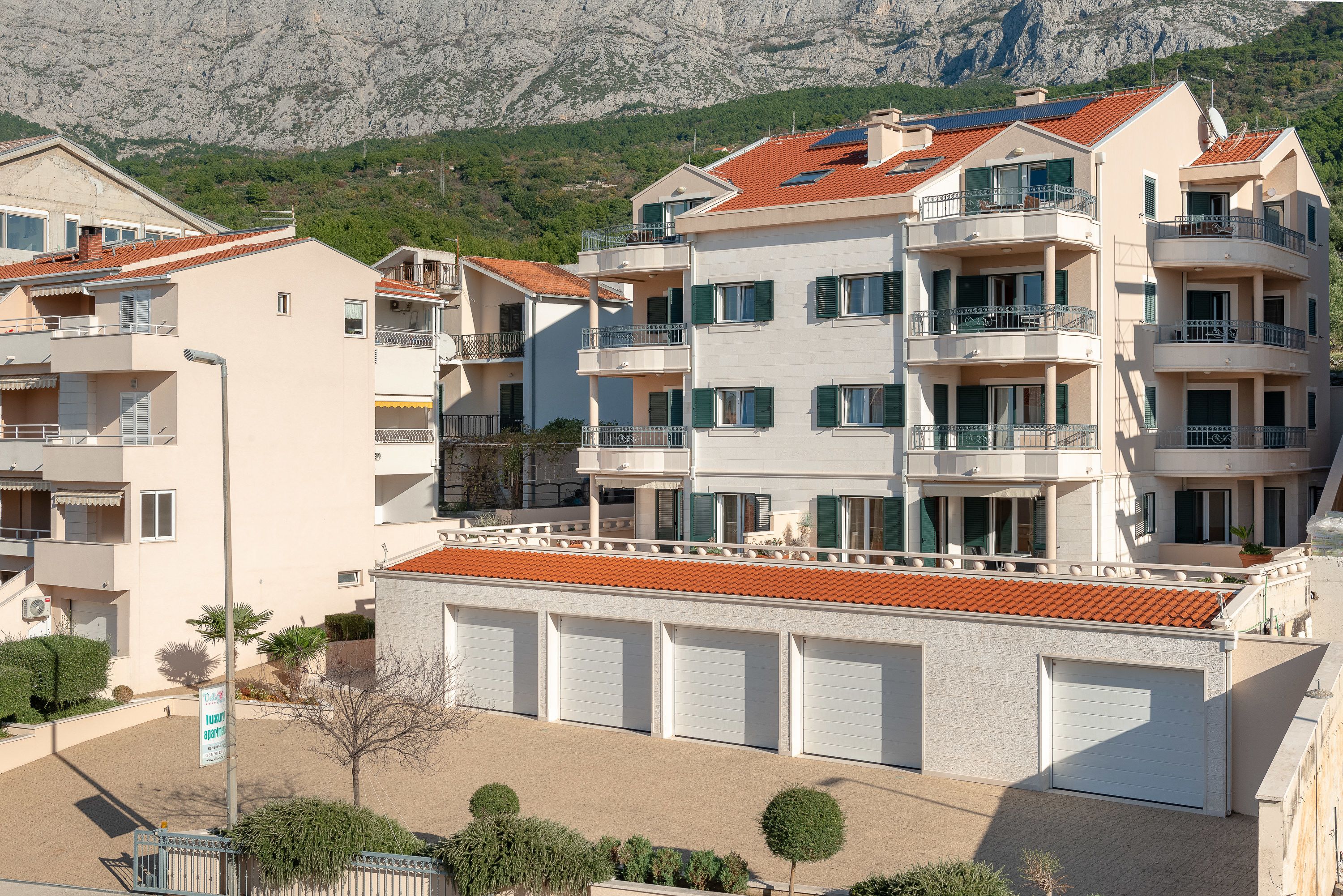A multi-story residential building with balconies, a red-tiled roof, and a garage area.