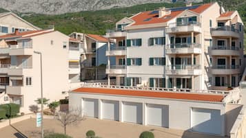A multi-story residential building with balconies, a red-tiled roof, and a garage area.