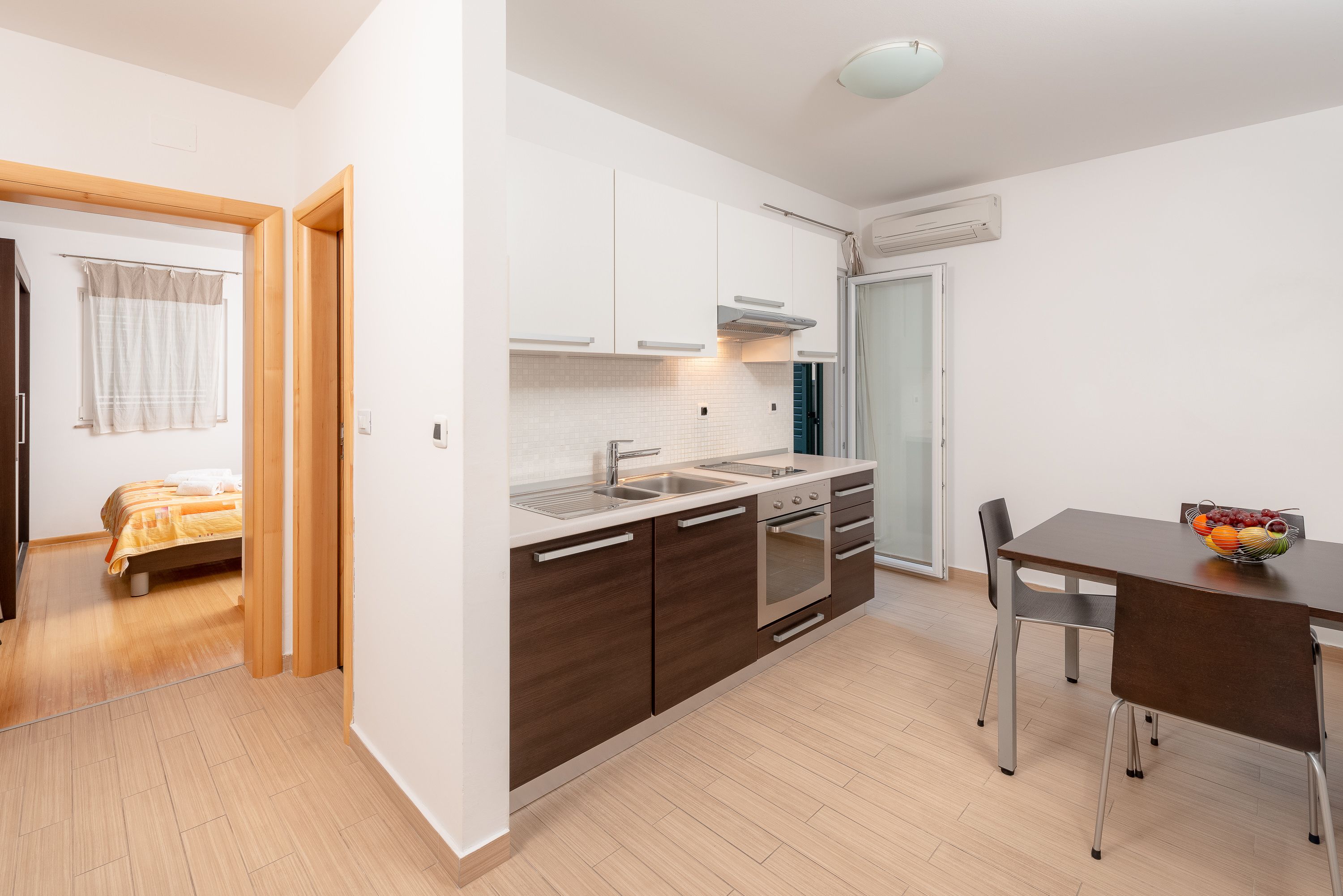 Une cuisine compacte dotée d’appareils électroménagers modernes, un coin repas avec une table et des chaises, et un lit visible dans la pièce adjacente.