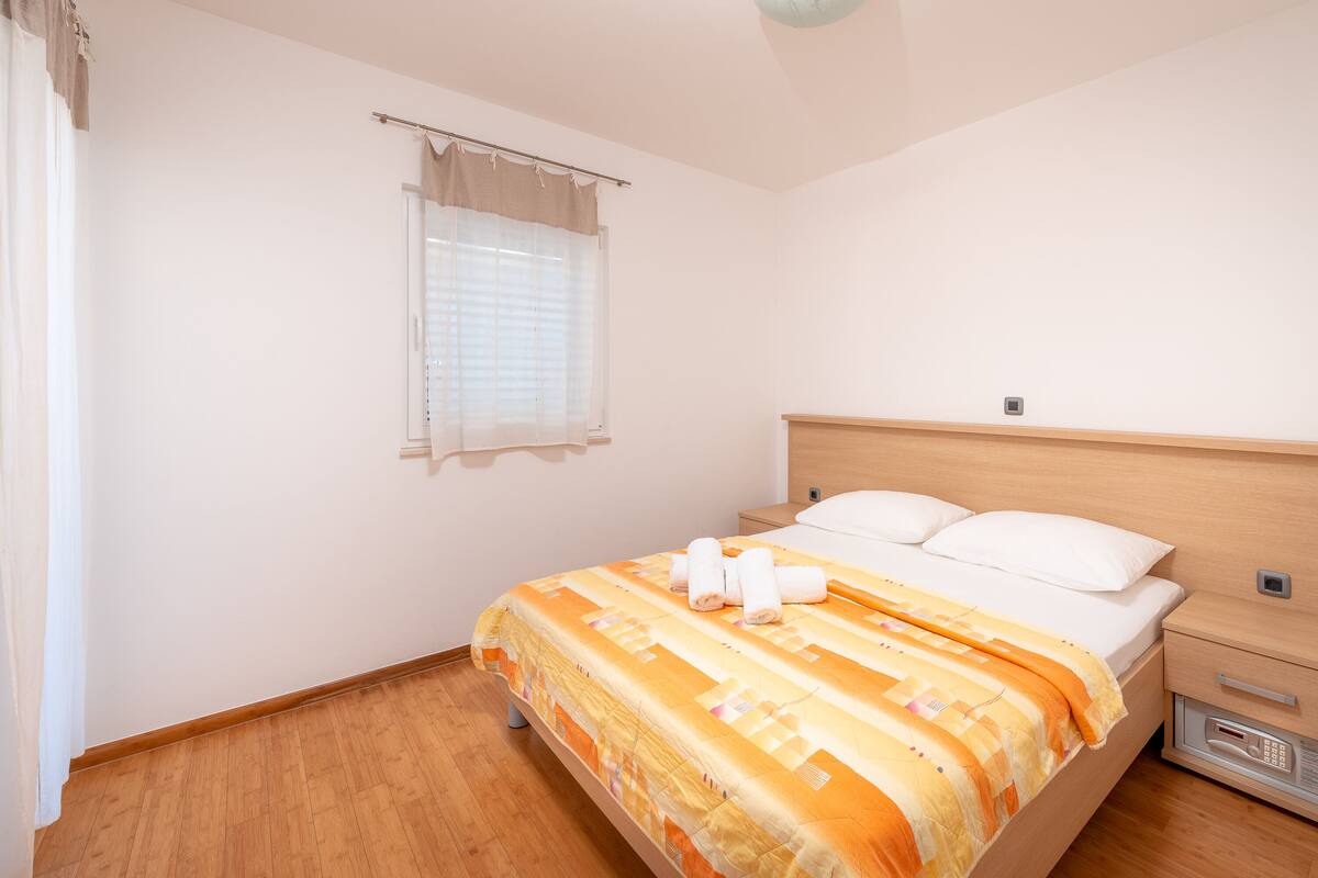 Ein Schlafzimmer mit einem hölzernen Bett, weißer Bettwäsche, einem Nachttisch und einem Fenster mit Jalousien.