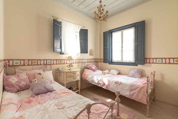 Un dormitorio con dos camas, un tocador, una mesita de noche y una ventana con contraventanas azules.
