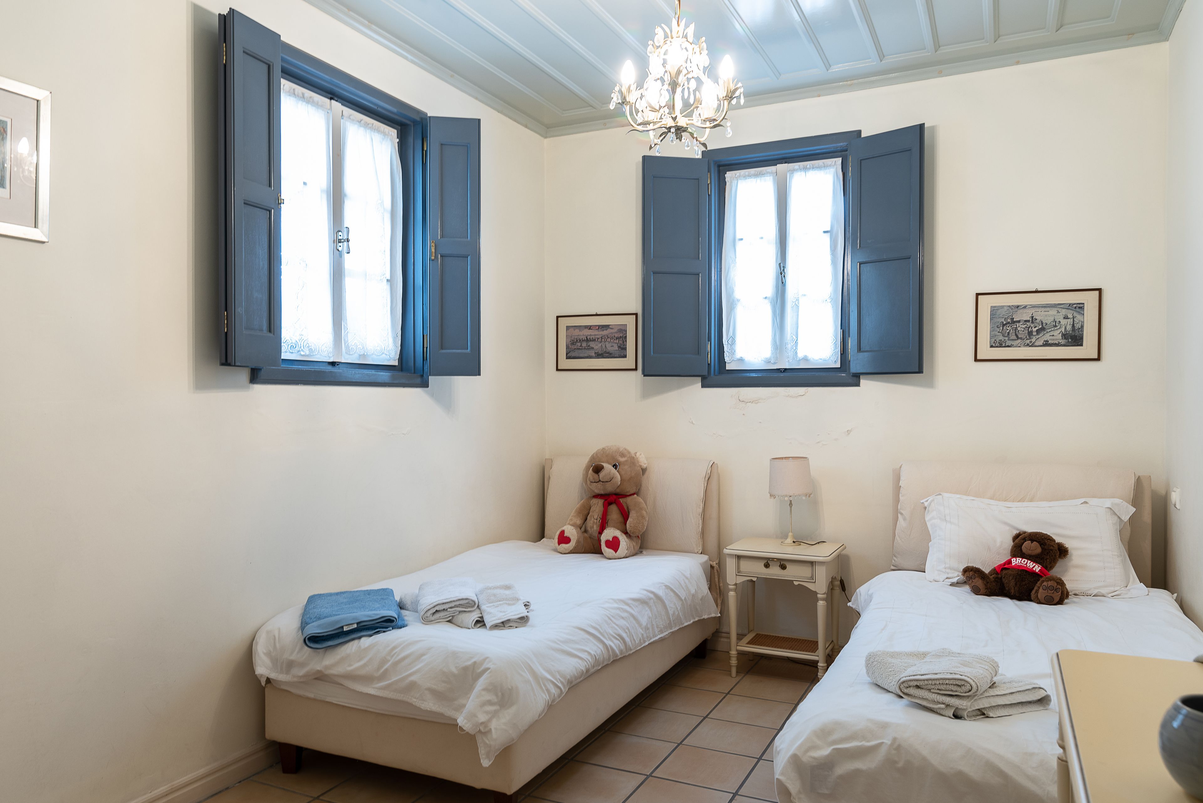 Ein Schlafzimmer mit zwei Betten, einer Kristallleuchter und einem Fenster mit blauen Fensterläden.