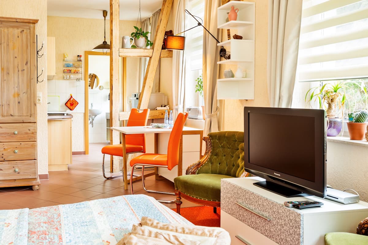 A cozy living room with a television, a green armchair, and a dining area with orange chairs.