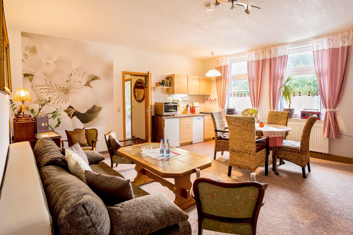 A cozy living room with a sofa, chairs, a dining table, and a kitchen in the background.