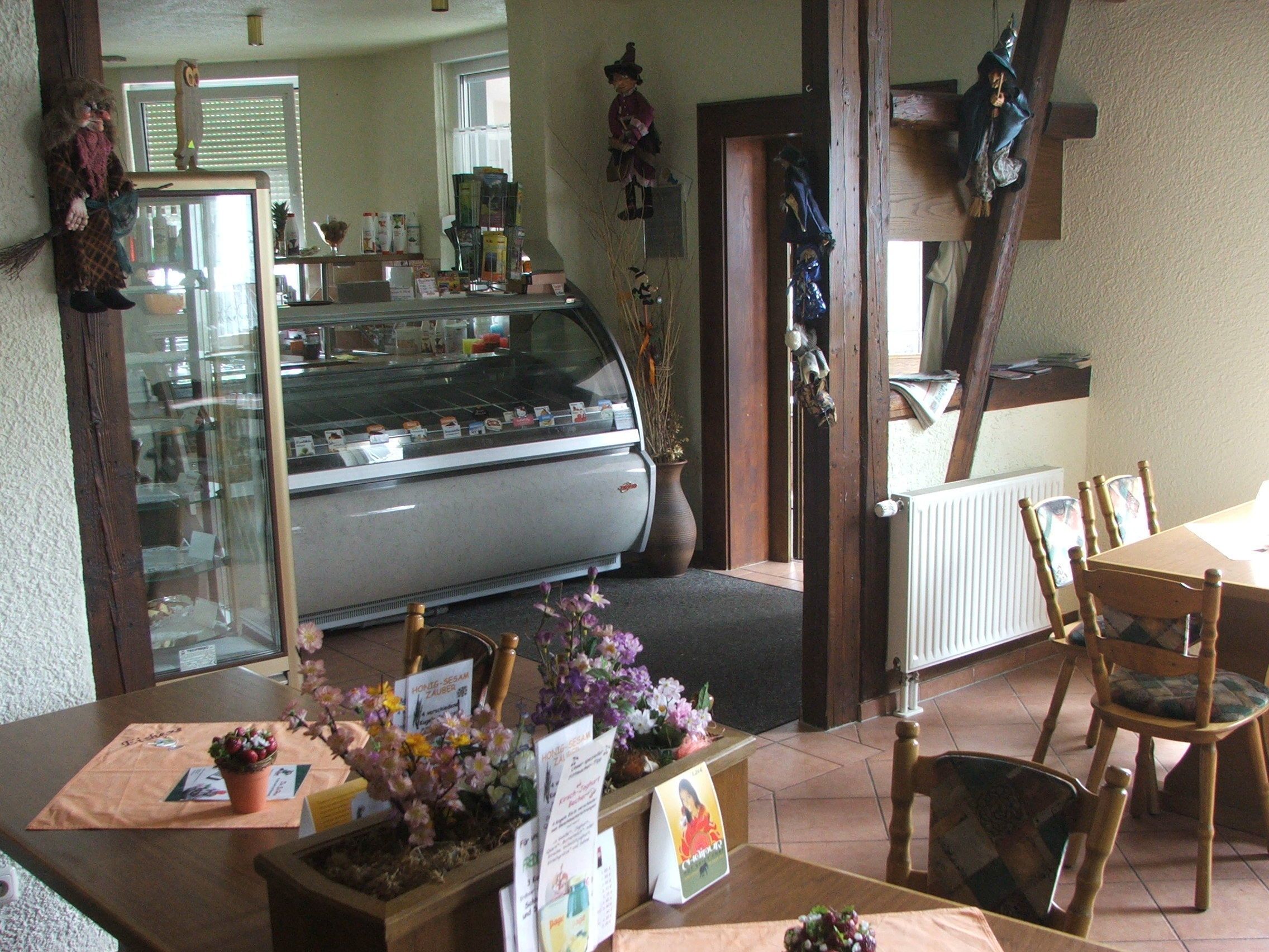 A cozy restaurant interior with a display case, wooden chairs, and a table with a placemat and flowers.