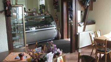 A cozy restaurant interior with a display case, wooden chairs, and a table with a placemat and flowers.