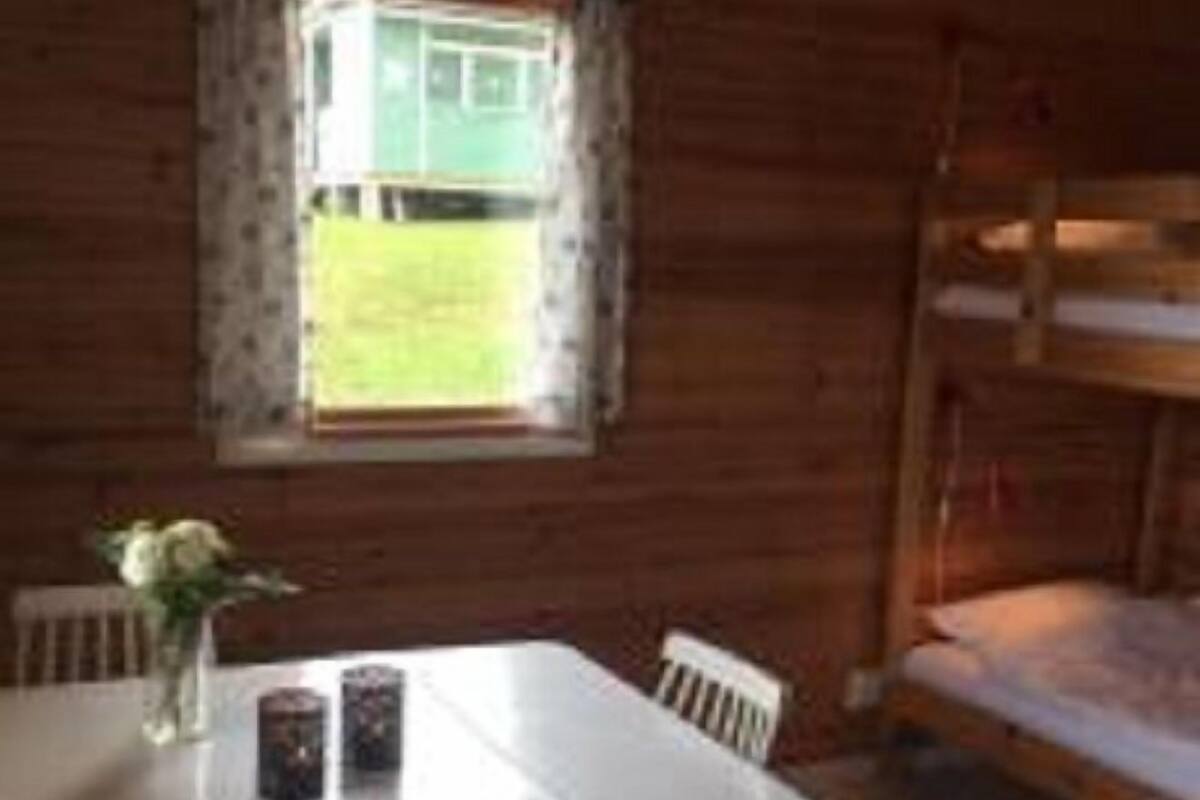 A wooden cabin room with a bunk bed, a table with chairs, and a window with a view of a green field.