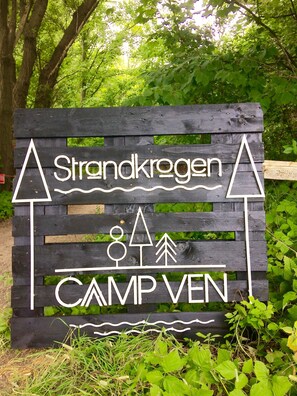 A wooden sign with 'Strandkrogen' and 'CAMP VEN' written on it, surrounded by greenery. - Camp Ven (Sankt Ibb)