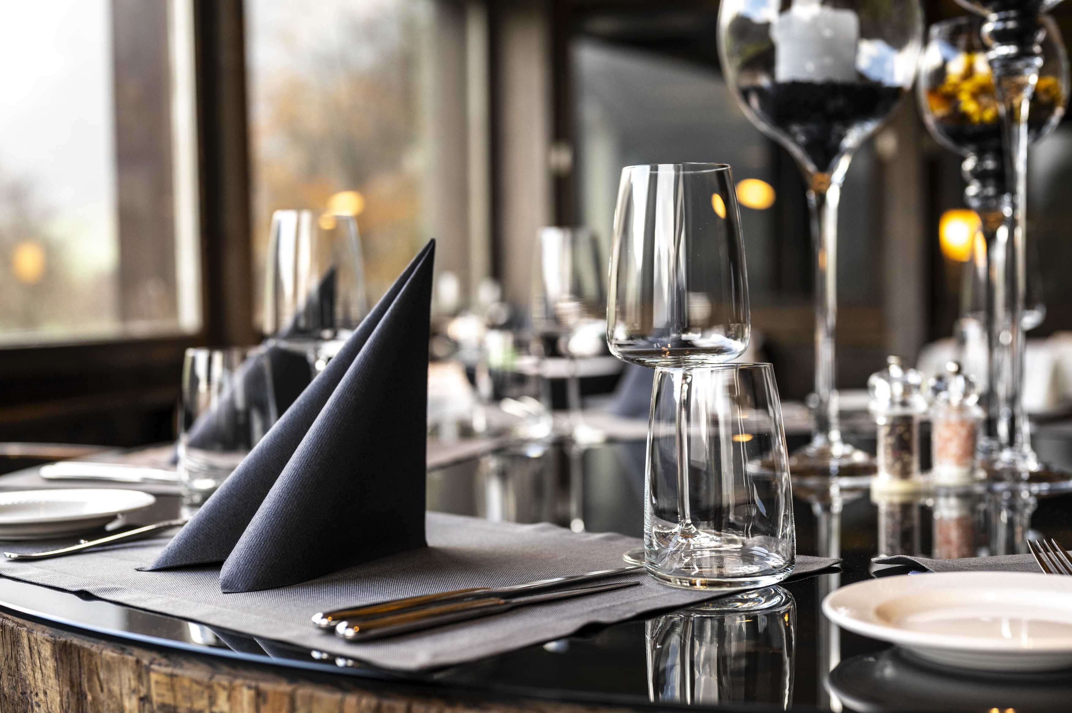 A dining table set with clear glassware, napkins, and cutlery.