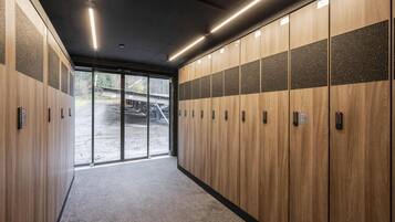 A modern locker room with wooden lockers, a glass door leading outside, and a carpeted floor.