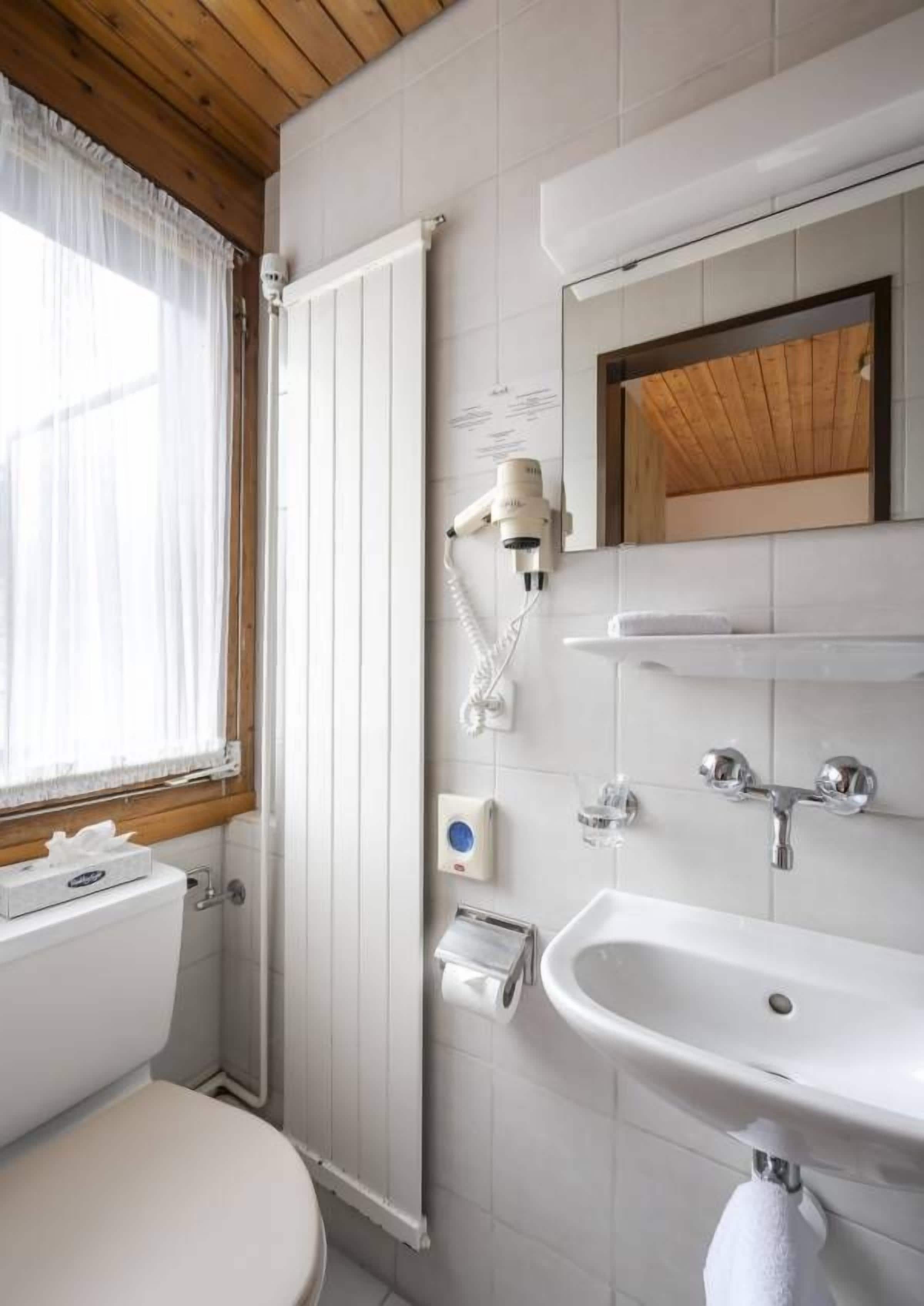 A bathroom with a toilet, a sink, a mirror, a towel rack, and a window with curtains.