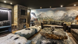 Una sala de estar moderna con chimenea de piedra, sofás de cuero y un gran mural de montañas en la pared.
