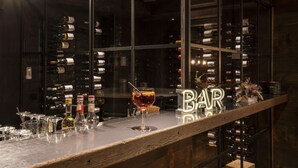 Zona de bar con una estantería para vinos al fondo, una copa de vino tinto sobre la barra y un letrero que dice