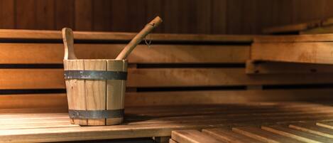 Banco de sauna de madera con un balde de madera que contiene un mazo de madera.