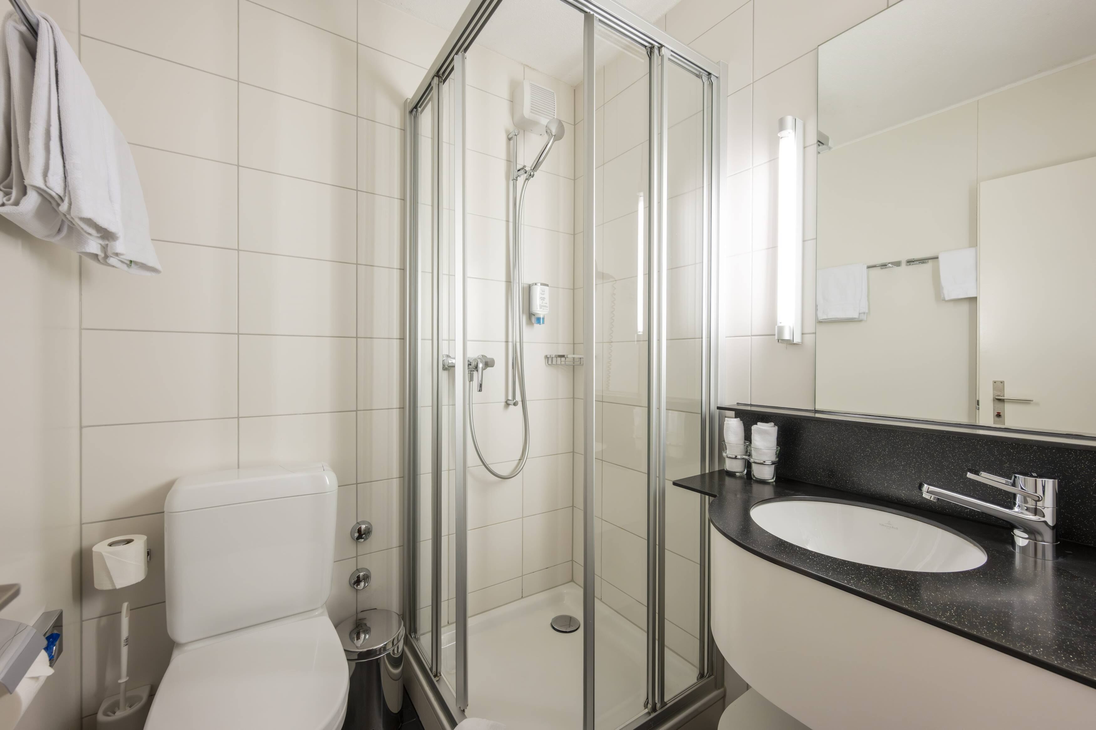Ein modernes Badezimmer mit einer Duschkabine aus Glas, einer weißen Toilette und einem schwarzen Waschtisch.