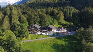 Un hotel con restaurante y banco situado en un valle boscoso, con una montaña al fondo.