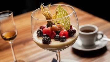 A dessert in a glass on a wooden table, accompanied by a cup of coffee and a glass of wine.