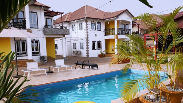 A swimming pool with a yellow inflatable ring, surrounded by lounge chairs and potted plants. - Candice serviced Apartment (Sunyani)