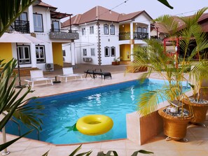 A swimming pool with a yellow inflatable ring, surrounded by lounge chairs and potted plants. - Candice serviced Apartment (Sunyani)