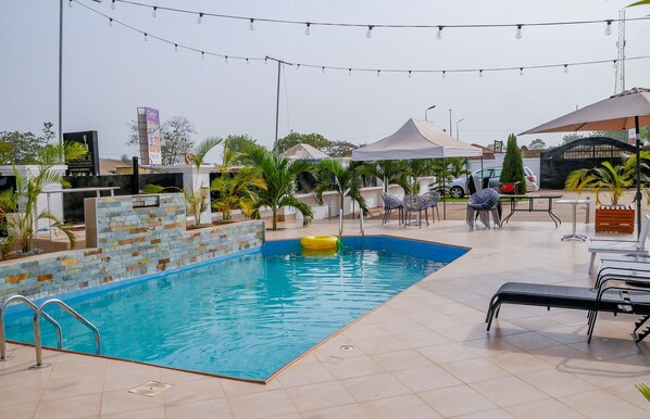 A swimming pool with a tiled deck, surrounded by lounge chairs and umbrellas, with a clear sky overhead.